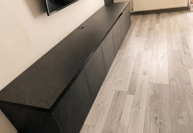 Detail hrany plávajúcej TV zostavy s priebežným kamenným dekorom a prievlakom na kábel
